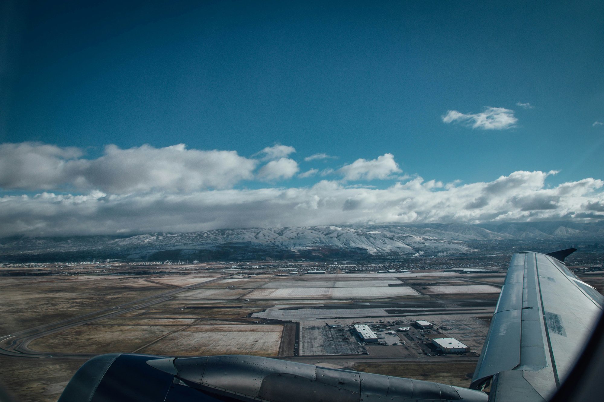 The view from a window seat on approach, a wing over snow-dusted mountains.