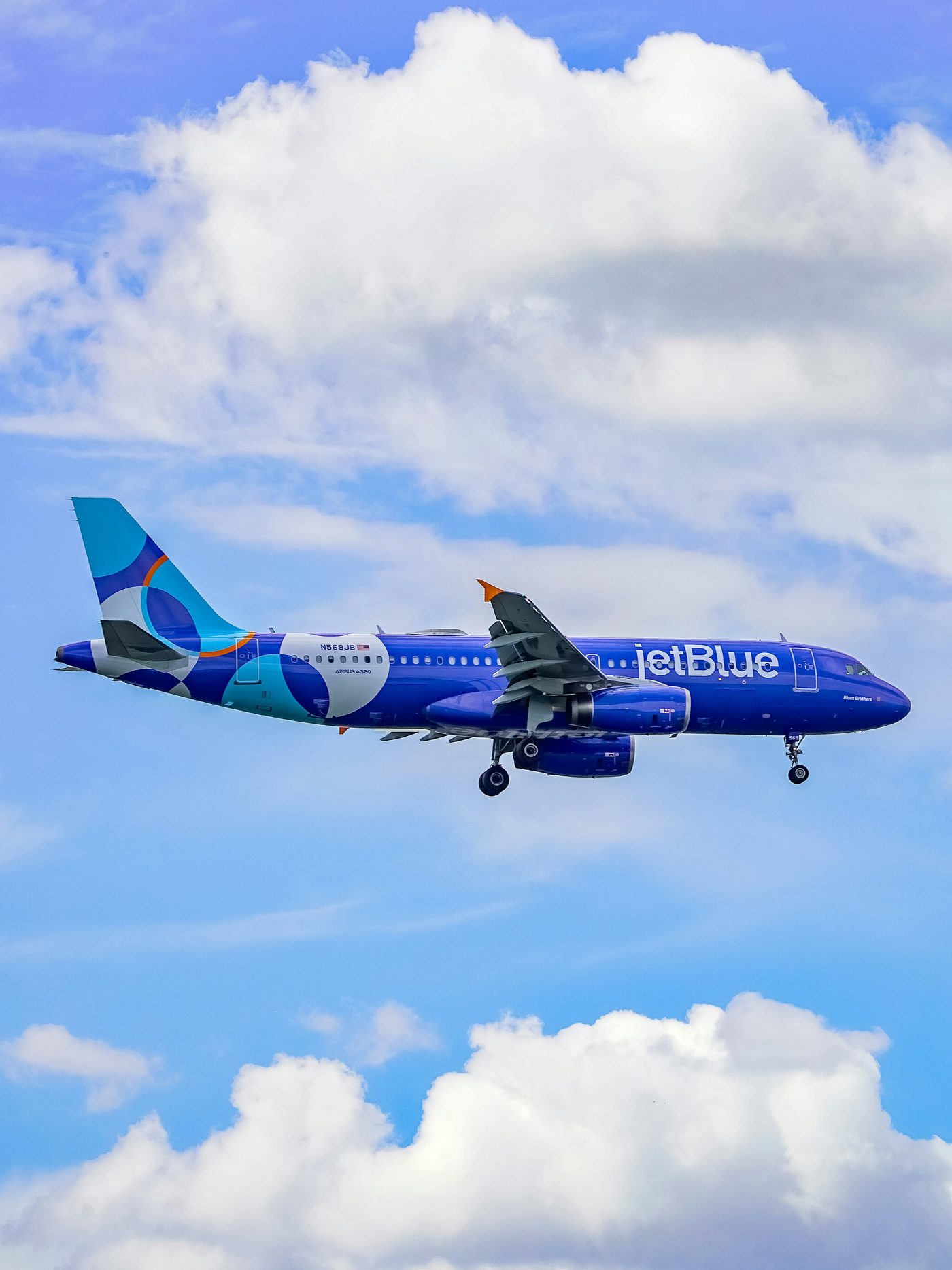 A JetBlue aircraft on approach against a blue sky.